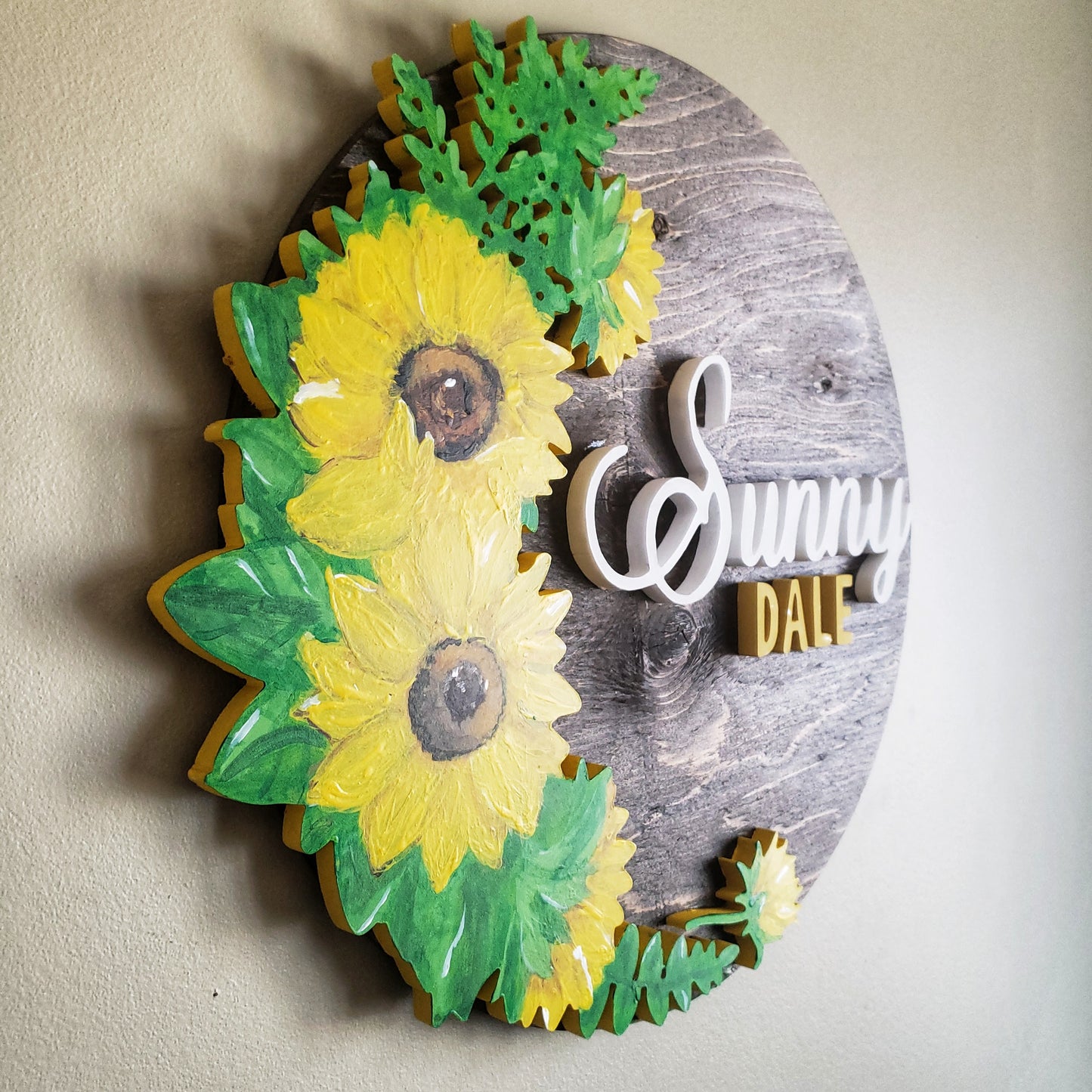 Medium stained round wood sign, with the name Sunny (in white) Dale (in yellow) with a large half wreath of sunflowers on the whole left side.