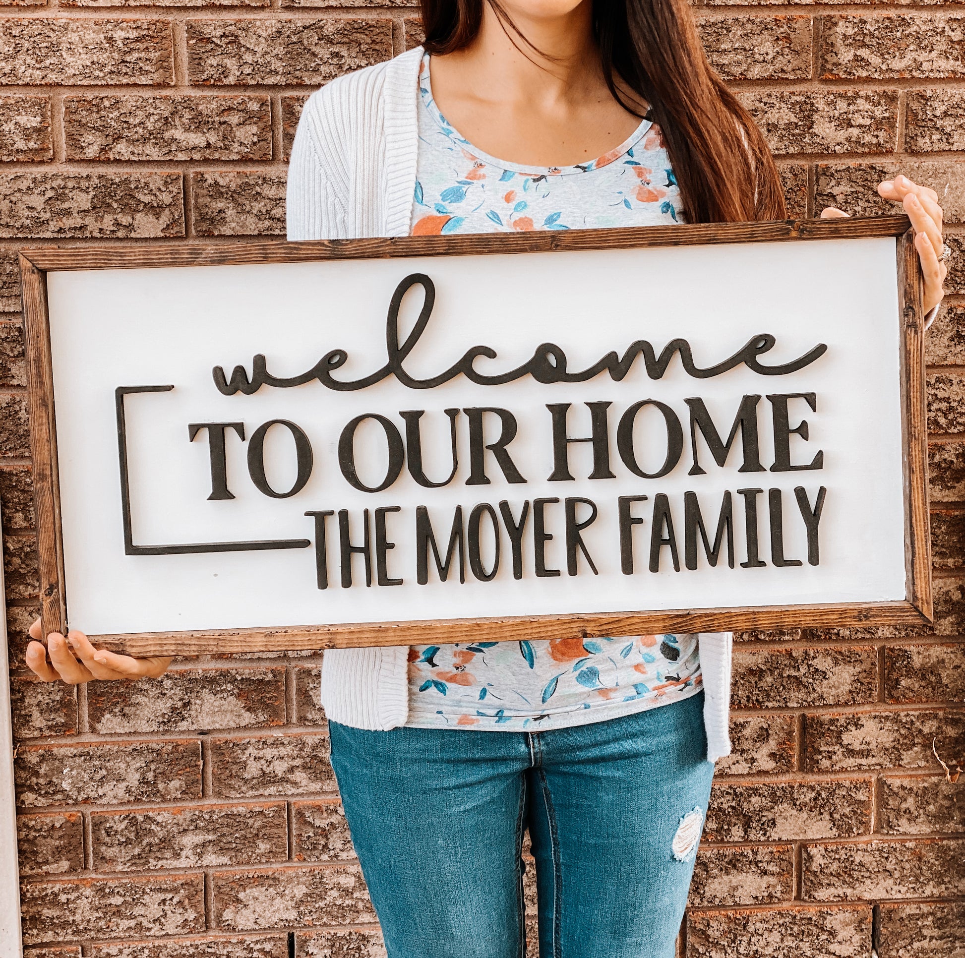 Rectangle sign with dark wood trim, white background and wording Welcome to our home, the Moyer Family