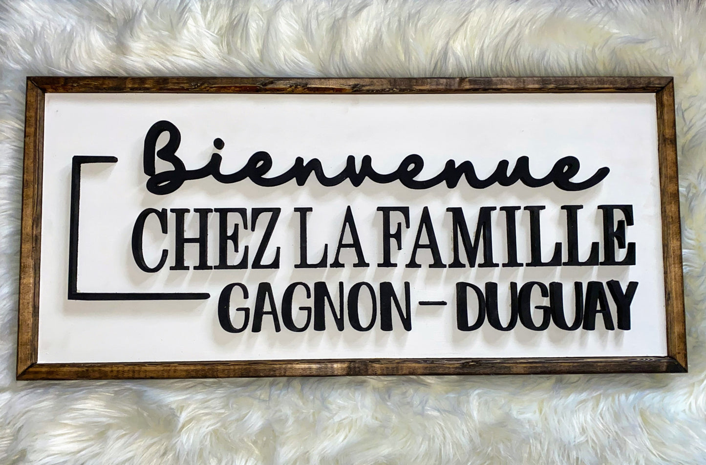 Rectangle sign with dark wood trim, white background and wording Bienvenue Chez la famille Gagnon-Duguay in black