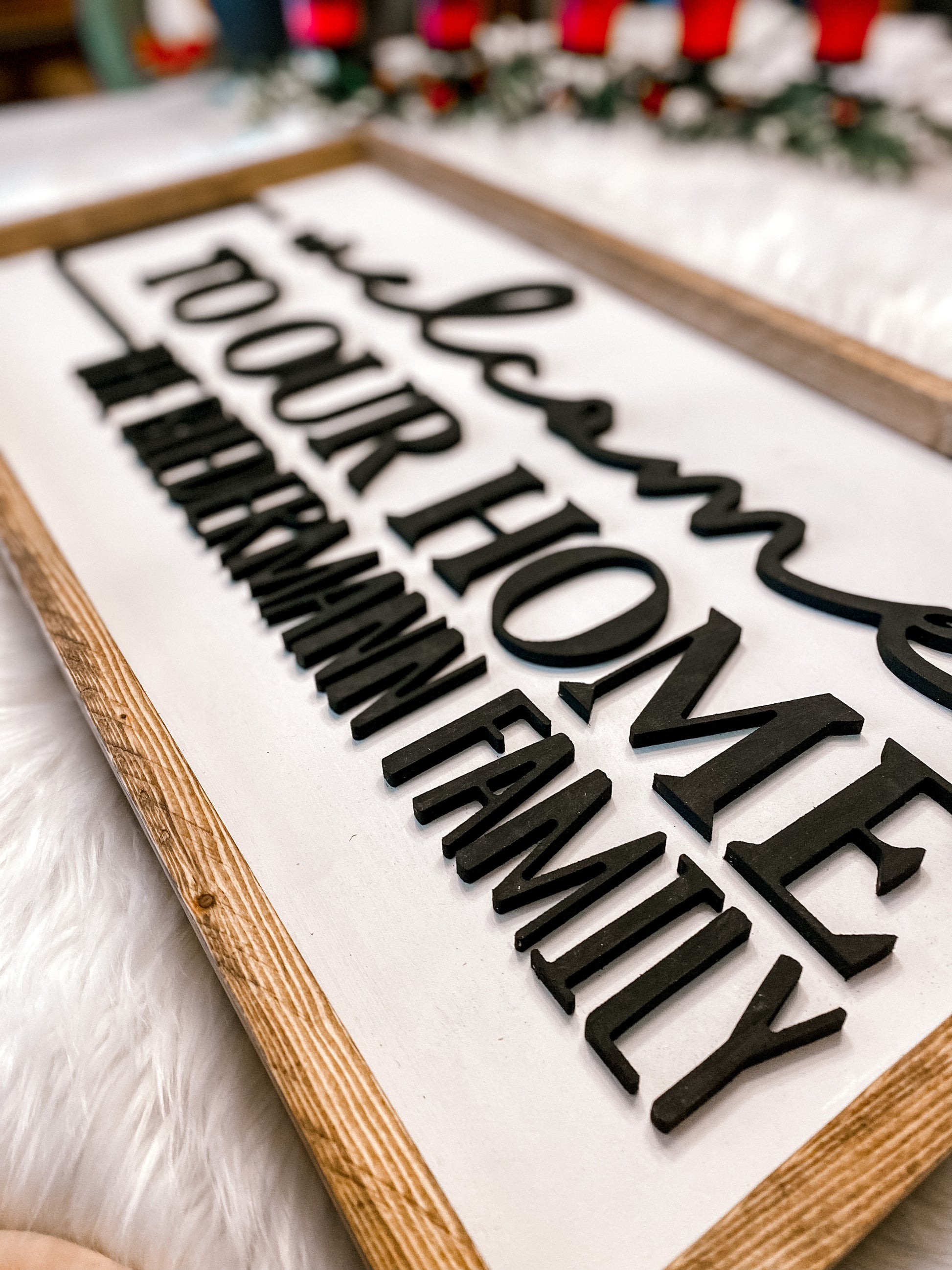 Rectangle sign with dark wood trim, white background and wording Welcome to our home, the biedermann family in black
